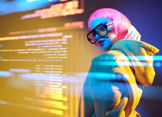 Modern girl with bright pink hair poses in yellow sunglasses and yellow suit in mixed color light with digital holograms. Virtual reality, digital technologies.